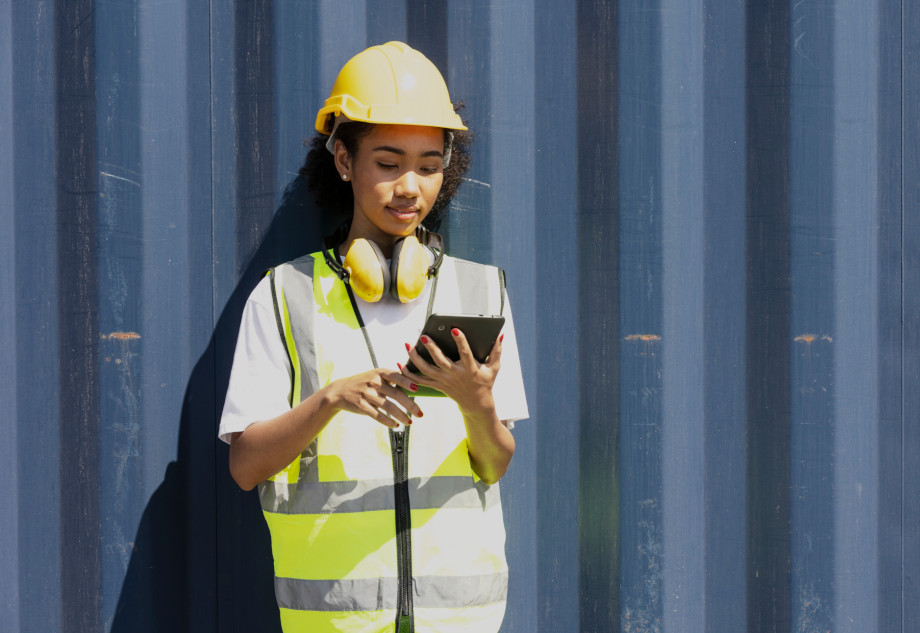 Female employee of a port looking at a tablet in front of a container